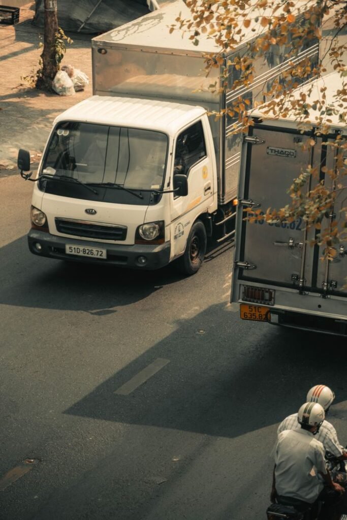 Aerial view of urban street with trucks and scooter riders, showcasing daily city life.