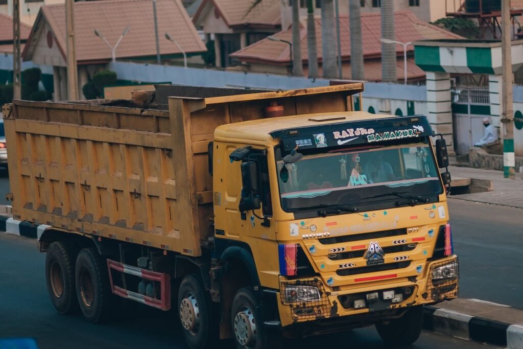 Large yellow dump truck driving through a city street in an urban setting.