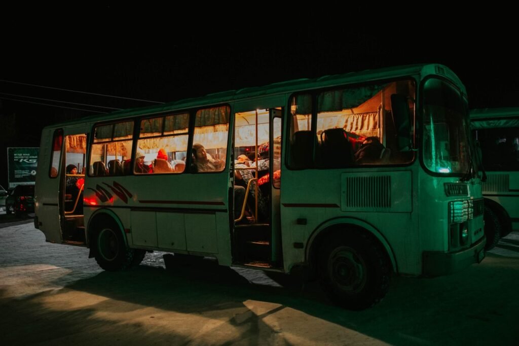 A bus parked at night with passengers visible inside, creating a warm, inviting glow.